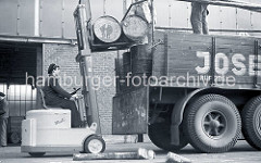 Der Fahrer des Gabelstaplers "Muli" hebt mit der Gabel des Flurfördergeräts zwei Tonnen auf die Ladefläche des Lastwagens am Togokai des Südwesthafens. Zwei Arbeiter verladen die Tonnen auf dem Lastkraftwagen.