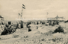 Historisches Foto vom Ostseestrand in Brunshaupten / Kühlungsborn;  Strandkörbe sind aufgestellt - Sandburg mit dem Schriftzug Bergmannsheil.  Touristen stehen  in Straßenkleidung  im Sand, im Hintergrund das Badehaus vom Herrenbad.