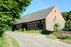 Fachwerkscheune mit großen Holztoren und Feldsteinmauer an der Brodowiner Straße von Oderberg -  die Straße ist mit Kopfsteinpflaster befestigt.