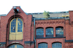 Historische Industriearchitektur, Fabrikgebäude der New-York Hamburger Gummi-Waaren Compagnie in Hamburg Harburg.  Dachwinde mit Eisenhaken am Giebel eines Lagergebäudes - eine kleine Kiefer wächst in der Regenrinne des Backsteinspeichers.