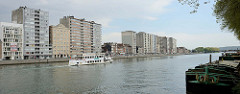 Hochhäuser am Ufer der Maas in Lüttich / Liège. Ein Fluss-Shuttle / La navette fluviale fährt die Maas flussabwärts. Rechts liegen Binnenschffe am Quai Godefroid Kurth.