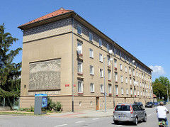 Grauer Wohnblock  in der Straße Čechova von  Budweis / České Budějovice - an der Hausfassade befindet sich ein Wandbild/Fresko mit einer Szene aus der Fischerei / Fischfang.
