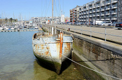 Hafenfront des alten Fischereihafens in Seebrügge, ein Holzboot liegt am Kai - mehrstöckige Gebäude mit Ferienwohnungen stehen an der Hafenpromenade.