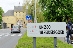 Schild Brugge UNESCO werelderfgoed - Welterbe, im Hintergrund das Smedenpoort / Schmiedetor; Teil der historischen Stadtbefestigung.