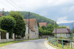 Dorfstraße entlang des Baches Kamionka in Pieszyce / Peterswaldau; einzelne Wohnhäuser - im Hintergrund bewaldete Berge vom Eulengebirge.