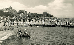 Alte Fotografie vom Badestrand in Kühlungsborn an der Ostsee, Badegäste mit Kindern spielen im Wasser - am Strand stehen Strandkörbe in Sandburgen. An der Promenade des Ostseebades Hotels und Villen.