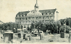 Historische Fotografie vom Kurhaus in Brunshaupten an der Ostsee; am Strand stehen Strandkörbe in Sandburgen, eine Frau liegt bekleidet auf einer Liege in der Sonne.