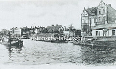 Historische Hafenszene am Finowkanal in Eberswalde, Arbeitsboote liegen am Kai - ein Frachtkahn wird auf dem Wasser gezogen.