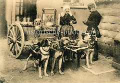 Milchhändlerin mit Haube - Polizist bei der Kontrolle; vier Hunde sind in der Deichsel des Karrens eingespannt.