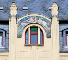 Denkmalgeschützte Fassade/Giebel eines Jugendstilgebäudes an der Wallstraße in Altenburg; bemalte Kacheln mit einem nackten Paar im Wald. Der Mann hat einen Fisch im Ketscher gefangen, die Frau trägt einen Blumenkranz im Haar.