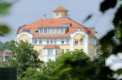 Blick über den großen Teich zur aufwändig restaurierten, denkmalgeschützten ehemaligen Gaststätte Stadt Dessau. Das Gebäude wurde 1910 erbaut und in DDR-Zeiten von der sozialistische Handelsorganisation (HO) als  Schnellimbiss "Gastronom" betrieben.