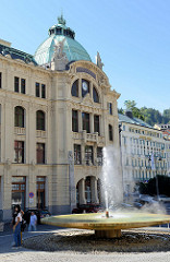 Sprudel, Springbrunnen / Vřídlo an der Straße Vřídelní in Karlsbad /  Karlovy Vary. Im Hintergrund das Jugendstilgebäude der Stadtsparkasse - eröffnet 1906 - Architekt Otto Stainl.