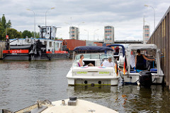 Sportboote und ein Schubschiff mit einem beladenen Containerleichter liegen in der Schleusenkammer der Schleuse Geesthacht an der Elbe.