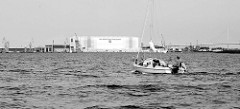 Ein Segelboot fährt mit Motorkraft auf dem Strelasund Richtung Stralsund;  im Hintergrund die Rügenbrücke und die Werfthalle der MV Werften.