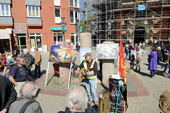 Ostermarsch 2019 - Demo für Abrüstung in Hamburg. Bänkelsänger mit politischen Antikriegsliedern - Bronzeskulpturen der Kreuzigungsgruppe vor der  Dreieinigkeitskirche von Hamburg St. Georg.