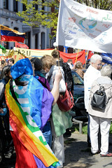 Ostermarsch 2019 - Demo für Abrüstung in Hamburg.  Eine Frau ist in die Regenbogenfahne Peace eingehüllt und schwngt eine weisse Fahne mit den Aufschriften Frieden in unterschiedlichen Sprachen.