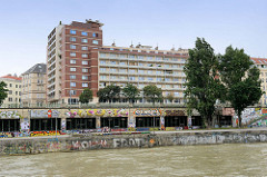 Mit buntem Graffiti versehene Mauern am Ufer des  Donaukanals in Wien - Blick auf die Wohnhausanlage Leopold Fige Hof am Franz-Josefs-Kai in Wien, errichtet 1967 - Areal des ehem. Hotels Métropole.