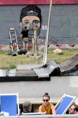 Ein Graffiti-Künstler arbeitet an einem Portrait an der Kaimauer vom Donaukanal in Wien.