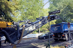 Bilder aus dem Hamburger Stadtteil Dulsberg - Bezirk Hamburg Nord. Straßenbauarbeiten im Alten Teichweg -  eine Asphalt-Straßen-Fräsmaschine trägt den Asphalt ab und fördert den Straßenbelag per Förderband auf einen bereitstehenden Lastwagen.