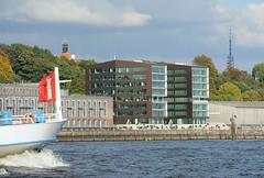 Elbuferbebauung - modernes Bürogebäude an der Grossen Elbstrasse. Auf dem Elbberg der Turm der Christianskirche - im Hintergrund der Hamburger Fernsehturm. Links der Bug eines Fahrgastschiffs der Hafenrundfahrt mit einer Hamburg Fahne.