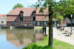 Teterow  ist eine Stadt im Landkreis Rostock in Mecklenburg-Vorpommern; Blick über den Mühlenteich zur historischen Stadtmühle an der Mühlenstraße - Sitzbänke am Wasser in der Sonne.