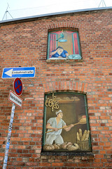 Teterow  ist eine Stadt im Landkreis Rostock in Mecklenburg-Vorpommern; Ziegelfassade / Fensterbilder mit Bäcker und Brot - Nachbarin am Fenster mit Katze und Vogelkäfig.