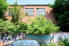 Fotos aus dem Hamburger Bezirk und Stadtteil Wandsbek; Industriearchitektur hinter einer mit Graffiti versehenen Steinmauer, Fliederbüsche.